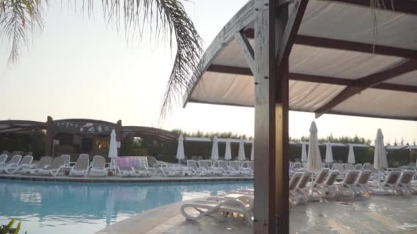 De zon schijnt boven het zwembad met kristalhelder water. Rijen witte ligbedden die langs het zwembad verblijven. Rustig resort in Turkije. — Stockvideo