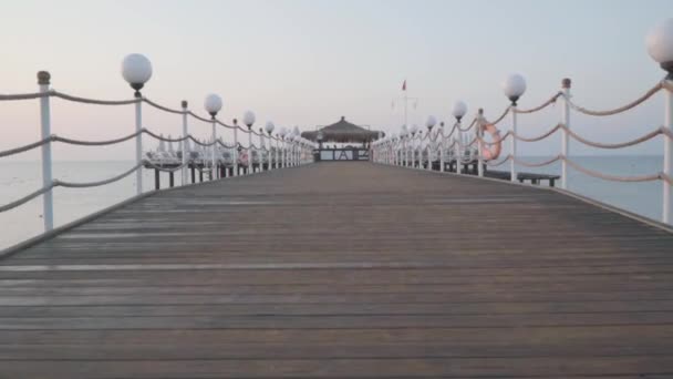 Cámara moviéndose hacia adelante a lo largo de la rampa de playa de madera. Grupo de personas bailando al fondo. Día de verano en el centro turístico oriental. Hermosa naturaleza turca . — Vídeos de Stock