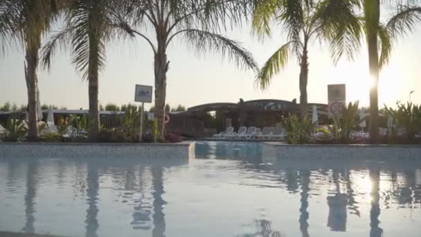 Sol de la mañana o de la noche reflejándose en el agua cristalina de la piscina. Tumbonas blancas vacías en el fondo. Hermoso complejo tranquilo sin gente. Descanso perfecto en Turquía . — Vídeo de stock