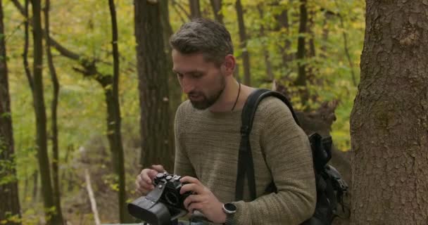 Manlig vit turist sitter i höstskogen med sin kamera och pratar. Självsäker gråhårig stilig man som tillbringar fritid utomhus. Film 4k Prores Hq. — Stockvideo