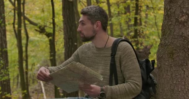 Vue latérale du beau touriste caucasien debout dans la forêt d'automne entre les arbres, regardant à travers la carte, et secouant la tête. Un homme confiant qui choisit la voie à suivre. Cinéma 4k séquences ProRes HQ . — Video