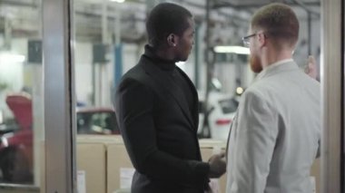 Genç, Afrika kökenli Amerikalı bir araba satıcısı başarılı, beyaz saçlı, takım elbiseli bir adama anahtar veriyor. Gözlüklü kızıl saçlı adam galeriden yeni araba alıyor. Araba bayiliği, araba işi..
