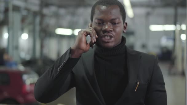 Уверенный афроамериканец, стоящий в автосалоне и разговаривающий по мобильному телефону. Молодой успешный продавец обсуждает деловую сделку. Автосалон, автобизнес . — стоковое видео