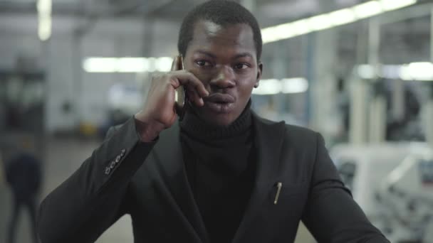 Portrait de jeune homme afro-américain beau parlant sur téléphone portable dans la salle d'exposition de la voiture. Jeune homme d'affaires qui parle d'achat d'automobiles. Concessionnaire automobile, entreprise automobile . — Video