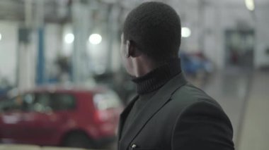 Çekici Afrikalı Amerikalı adamın portresi yeni arabalara bakıyor ve kameraya bakıyor. İşyerinde kalan başarılı genç bir araba satıcısı. Araba bayiliği, araba işi..