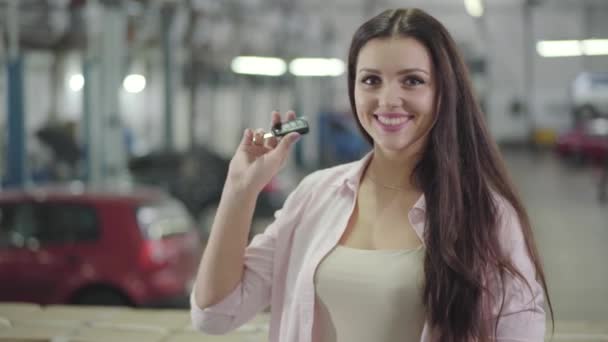 Feliz chica caucásica joven besando llaves del coche, aplaudiendo y sonriendo. Hermosa mujer que compra un automóvil nuevo en la sala de exposición de coches. Cliente feliz posando en concesionario de coches. Negocio del coche, cliente feliz . — Vídeos de Stock