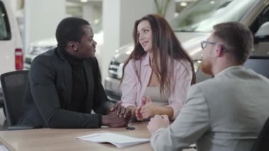 Başarılı Afrikalı Amerikalı iş adamı galerideki araba satıcısına banka kartı veriyor. Tatmin olmuş beyaz bir eş ona sarılıyor ve gülümsüyor. Çift ırklı çift yeni araba alıyor. Araba bayiliği, araba işi..