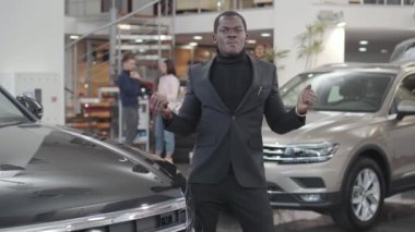 Yeni arabasının yanında araba anahtarlarıyla dans eden mutlu Afrikalı Amerikalı adam. Satın almakla övünen memnun bir adam. Galeride başarılı bir genç işadamı aracı satın alıyor. Araba bayiliği, araba işi..