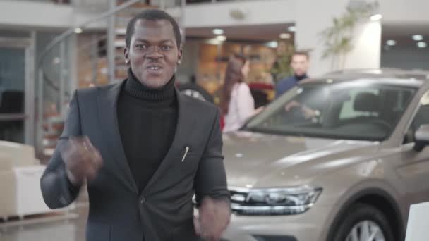 Närbild porträtt av glada afroamerikanska killen skryta bilnycklar framför kameran, gestikulera ja, och dansa. Glad säljare gör försäljning köp affär i showroom. Bilhandel, bilindustri. — Stockvideo