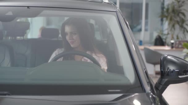 Çekici beyaz bir kız araba kuaföründe oturup dikiz aynasını kontrol ediyor. Galeride otomobil seçmekte başarılı bir iş kadını. Araba bayiliği, araba işi.. — Stok video