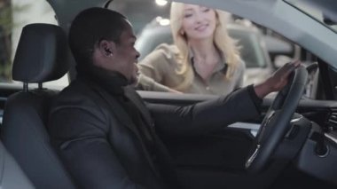 Bulanık beyaz kadın, kuaförde oturan Afrikalı Amerikalıya araba anahtarı veriyor. Memnun müşteri el kol hareketi yapıyor ve gülümsüyor. Galeride araba satan başarılı bir kadın araba satıcısı..