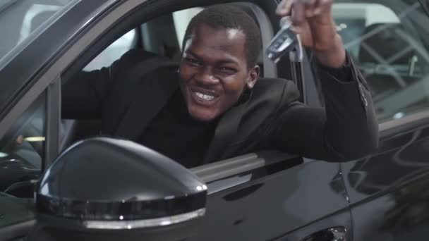Primo piano volto di felice uomo afroamericano seduto in salone di auto e vantarsi chiavi. Uomo d'affari di successo l'acquisto di nuove automobili nello showroom. Concessionaria auto, industria automobilistica . — Video Stock