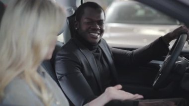 Sarışın, beyaz kadın satıcının müşterisiyle araba kuaföründe oturduğunu ve ona arabanın anahtarlarını verdiğini gördüm. Gülümseyen Afrikalı Amerikalı adam galeride yeni otomobiller alıyor. Araba bayiliği, araba işi..