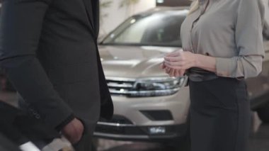 Afrika kökenli Amerikalı bir erkek, beyaz bir bayandan araba anahtarlarını alıyor ve evet işareti yapıyor. Başarılı bir iş adamı otomobil satın alıyor. Araba galerisi, araba işi. Satış ve alım..