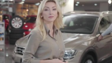 Sarışın, beyaz bir kadın kameraya dönüp arabanın anahtarlarını gösteriyor ve gülümsüyor. Başarılı bir iş kadını galeride yeni bir araba alıyor. Araba bayiliği, araba işi..
