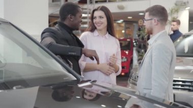 Genç çok ırklı çift galerideki satıcıdan araba anahtarlarını alıyor. Genç, güzel, beyaz bir kadın Afrikalı Amerikalı bir adama sarılıyor. Araba satıcısıyla el sıkışma işi. Araba bayiliği, araba işi..