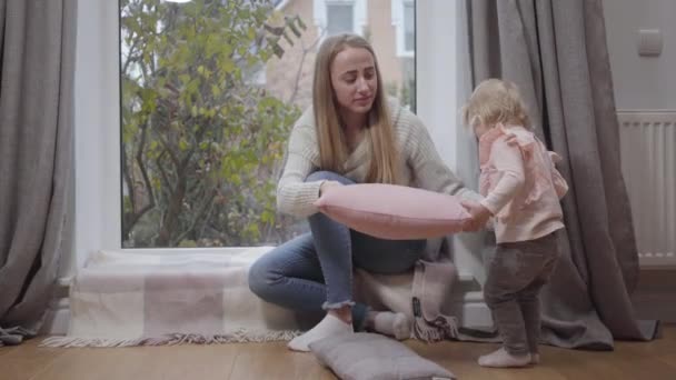 Jonge aantrekkelijke blanke vrouw zit bij lage vensterbank en praat met een klein meisje. Schattig kind in roze blouse lopend naar moeder. Familie brengt de herfstdag binnen door. Gelukkig ouderschap. — Stockvideo