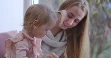 Kafkas anne ve bebek kızın yakın plan portresi. Evde oturup renkli kalemlerle çiziyorlar. Küçük kızını eğiten gülümseyen genç bir kadın. Sinema 4k görüntüleri Prores Hq.