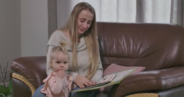 Jeune femme caucasienne joyeuse lisant le livre pour la petite jolie fille. Mère heureuse éduquant et divertissant sa fille adorable. Joie de la maternité, maternité heureuse. Cinéma 4k séquences ProRes HQ . — Video