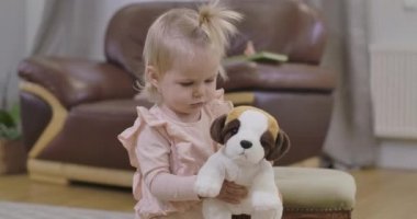 Yumuşak oyuncak köpekle kameraya doğru yürüyen güzel bir kızın portresi. Sarışın, koyu gri gözlü, sevimli çocuğun yakın çekimi. Sinema 4k görüntüleri Prores Hq.