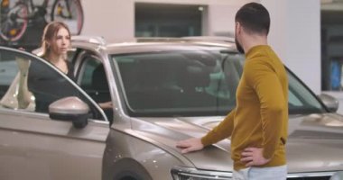 Güzel beyaz bir aile araba galerisinde duruyor ve yeni otomobilleri inceliyor. Otomobil galerisinden araç alan kendinden emin bir adam ve kadın. Araba galerisi, araba işi. Sinema 4k görüntüleri Prores Hq.