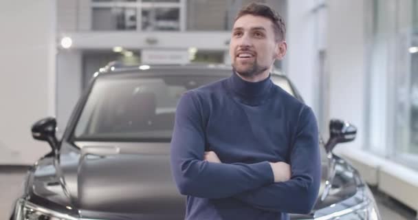 Retrato de primer plano del hombre caucásico satisfecho de pie frente a un coche negro nuevo. Cliente feliz con el vehículo comprado. Concesionario de autos, negocio de autos. Cinema 4k metraje ProRes HQ . — Vídeos de Stock