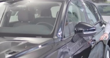 Yetişkin beyaz bir adam arabaya geliyor, dikiz aynasını okşuyor ve kuaföre giriyor. Zarif siyah arabasında kendinden emin bir araba sahibi. Araba galerisi, araba işi. Sinema 4k görüntüleri Prores Hq.