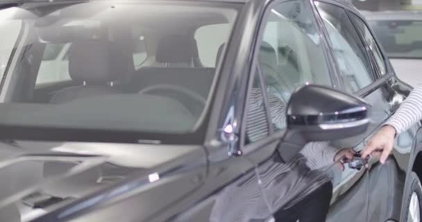 Γενειοφόρος Καυκάσιος ενήλικας πλησιάζει το αυτοκίνητο, ανοίγει την πόρτα, κάθεται στο σαλόνι, και προσαρμόζει τον καθρέφτη. Σίγουρος ιδιοκτήτης αυτοκινήτου στο κομψό μαύρο αυτοκίνητό του. Κινηματογράφος 4k πλάνα Prores Hq. — Αρχείο Βίντεο