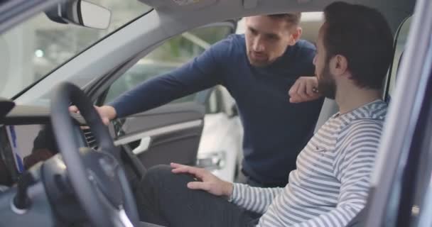 Vista lateral del concesionario caucásico del coche masculino que explica los detalles al cliente. Barbudo hombre exitoso comprando un vehículo nuevo en la sala de exposición. Concesionario de autos, negocio de autos. Cinema 4k metraje ProRes HQ . — Vídeos de Stock