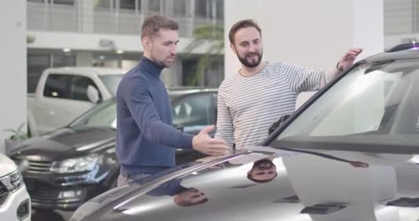 Retrato de dos hombres caucásicos de pie en el concesionario de automóviles y mirando el coche. Amigos eligiendo un vehículo nuevo. Alquiler de coches, negocio de coches. Cinema 4k metraje ProRes HQ . — Vídeos de Stock