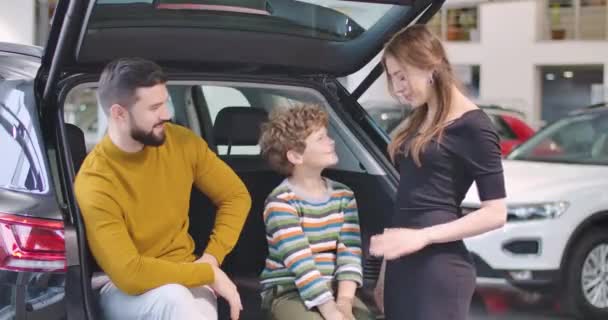 Successful Caucasian businessman sitting in big open car trunk and admiring his son playing clapping hands with his beautiful mother. Happy family renting vehicle. Cinema 4k footage ProRes HQ. — ストック動画