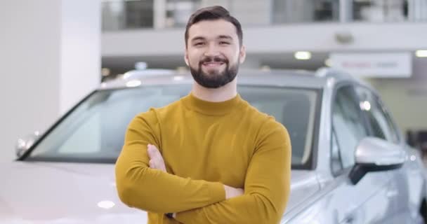 Портрет упевненого кавказького чоловіка в гірчичному светрі, що стоїть перед білою машиною. Щасливий власник або лісоруб на задньому плані нової машини. Машинний бізнес. Відеозапис фільму 4k Prores Hq. — стокове відео
