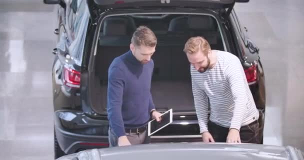 Vista superior op concesionario de coches caucásicos y cliente masculino examinando parachoques del coche. Comerciante explicar las ventajas de vehículo nuevo para el cliente. Negocio de coches, alquiler de coches, concesionario. Cinema 4k metraje ProRes HQ . — Vídeos de Stock