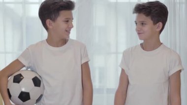 İki esmer beyaz ikiz kardeş birbirlerine bakıyor, kameraya dönüp gülümsüyorlar. Elinde futbol topu tutan öğrenci. Kardeşler spora gidiyor. Sağlıklı yaşam tarzı, fiziksel aktivite.