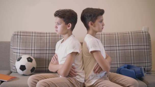 Profil portrétu dvou bělošských brunetových dvojčat sedících zády k sobě. Uražení bratři se otočili a dívali se jeden na druhého. Problémy s komunikací, nedorozumění. — Stock video