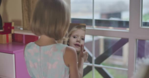 Rückansicht eines jungen kaukasischen Mädchens, das einen Spiegel in der Hand hält und lächelt. Kindergesichter spiegeln sich im Spiegel. Schuss über die Schulter. — Stockvideo