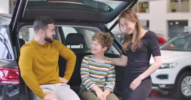 Der junge kaukasische Vater und die Mutter lächeln und umarmen ihren Sohn. glückliche Familie in Showroom Wahl neuer Automobil. Menschen, die ein Fahrzeug mieten oder kaufen. Autogeschäft. Kino 4k Filmmaterial prores hq. — Stockvideo