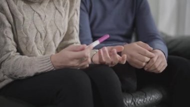 Kadın ve erkek ellerine yakın çekim. Kadın hamilelik testi tutuyor, beyaz adam ayağa kalkıyor ve uzaklaşıyor. Beklenmedik hamilelikle şok olmuş koca. İlişki sorunları.
