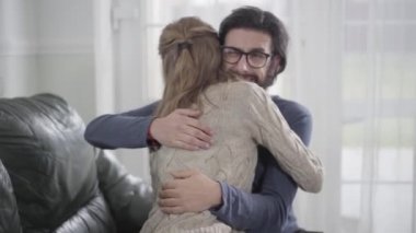 Gözlüklü, karısını kucaklayan mutsuz, beyaz bir adamın portresi. Kadın hamilelik testini onaylıyor ve sakallı adam mutluluğu taklit ediyor. Genç adam baba olmaya hazır değil..