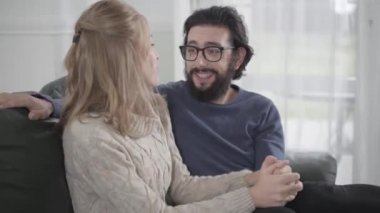 Sarışın sevgilisine ya da karısına sarılan genç beyaz adamın yakın plan portresi evde rahat bir kanepede oturuyormuş gibi. Gülümseyen aile hafta sonlarını evde birlikte geçiriyor..
