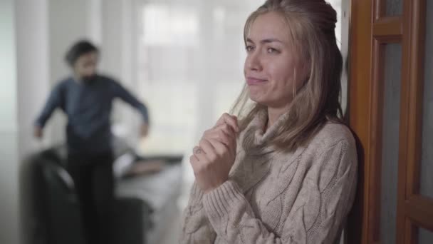Close-up face of exhausted Caucasian woman standing with pregnancy test, and crying. Blurred husband or boyfriend yelling at the background. Unwanted pregnancy, relationship problems. — 비디오