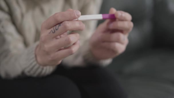 Sidovy närbild av kvinnliga kaukasiska händer som håller ett positivt graviditetstest. Kvinna med ormtatuering på fingret bestämmer vad man ska göra med oväntad graviditet. — Stockvideo