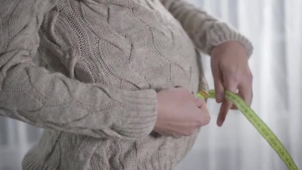 Boční pohled zblízka na ženské ruce měřící velikost pasu páskou, ukazující 97 cm a odhazující měřicí pásku. Těhotná běloška kontroluje změny v těle během těhotenství. — Stock video