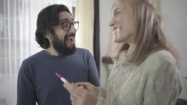 Retrato de familia caucásica feliz mirando la prueba de embarazo afirmativa, abrazos y besos. Futuros padres gozosos disfrutando de buenas noticias. Embarazo planificado, buena relación . — Vídeos de Stock