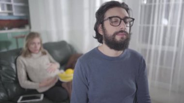 Gözlüklü, yorgun, beyaz bir adam arka plandan bağıran hamile karısı gibi surat yapıyor. Hasta adam kadınların ruh hali değişikliklerinden muzdarip. Hamilelik, gebelik, ruh hali değişiklikleri, sabır..