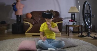 VR Google 'daki ciddi bir beyaz çocuğun portresi görünmez bir şey taşıyor. Sarı tişörtlü ve mavi kotlu öğrenci evde VR kulaklık kullanıyor. Z jenerasyonu, 3 boyutlu gerçeklik. Sinema 4k Prores Merkezi.