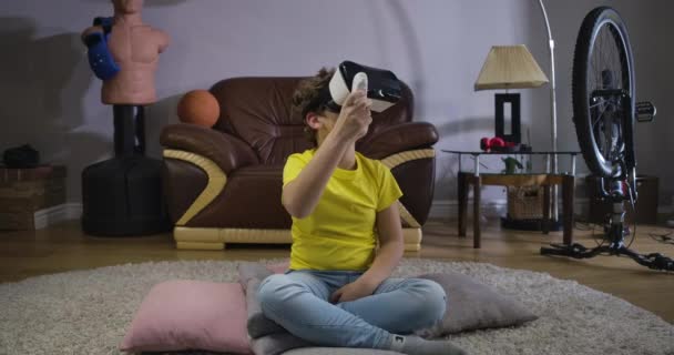 Homme adolescent caucasien portant casque VR en utilisant la télécommande pour jouer le jeu. Enfant regardant autour et souriant. Réalité augmentée, VR googles. Siège social Cinema 4k ProRes . — Video