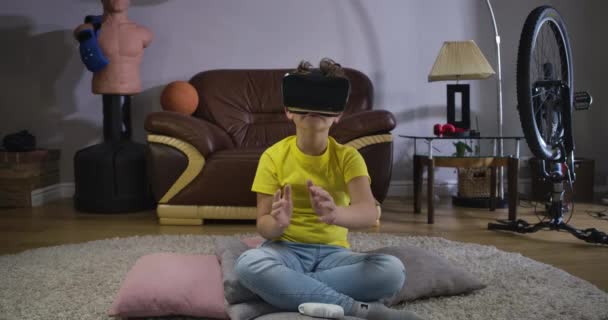 코카서스 출신 곱슬머리의 남자 아이는 VR 헤드셋을 사용하여 보이지 않는 것에 손을 댔습니다. 격식없는 옷을 입은 귀여운 남학생 이 집 의부드러운 카펫 위에 앉아 손을 움직 이는 것처럼 말이다. 3D 현실. 영화 4K 전립선 HQ. — 비디오