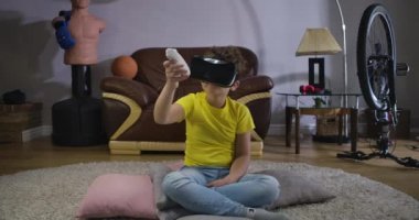 VR Google 'daki küçük çocuk uzaktan kumandayla elini hareket ettiriyor ve kontrolörün yönüne bakıyor. Kapalı alanda arttırılmış gerçeklik kullanan günlük giysili beyaz bir çocuk. Sinema 4k Prores Merkezi.