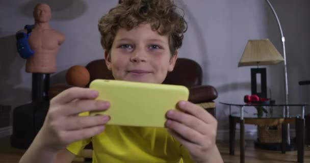 Крупный план портрета радостного кавказского мальчика, играющего в видеоигры. Веселый подросток в желтой футболке с помощью смартфона и глядя вперед. Онлайн игры, технологии, поколение z. Cinema 4k ProRes HQ . — стоковое видео